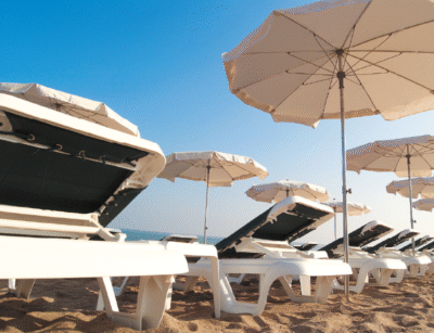 Lola sun loungers lined up under white umbrellas, with a clear sky