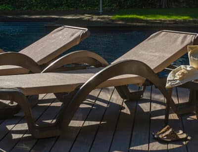 Two light-colored polypropylene resin sun loungers are seen next to a swimming pool