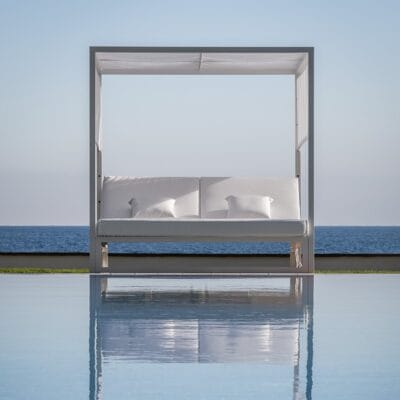 Cama balinesa moderna blanca con 2 colchónes individuales unidos de color blanco y almohadas a juego, diseño minimalista y elegante. Se ve de fondo el mar