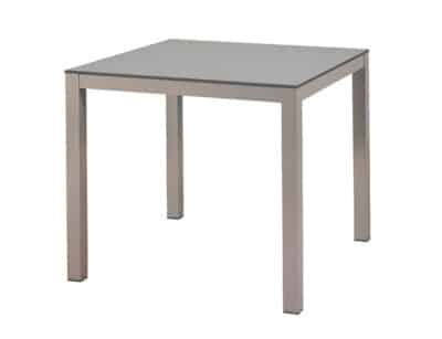 L'image montre une table carrée au design simple et moderne, avec une surface couleur colombe avec panneau HPL et quatre pieds en aluminium de couleur grise. Le style est minimaliste et élégant